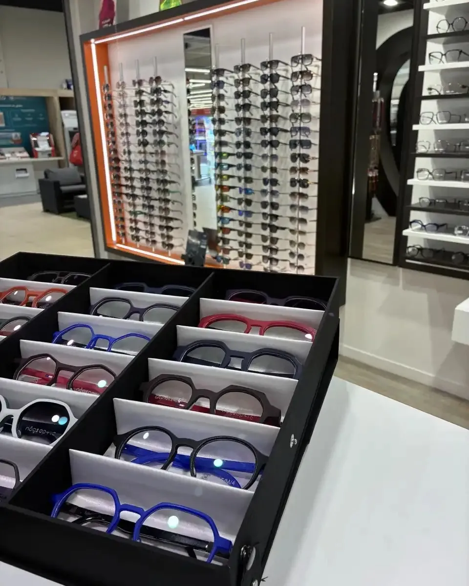 Coffret de montures colorées présenté devant le mur de lunettes de soleil